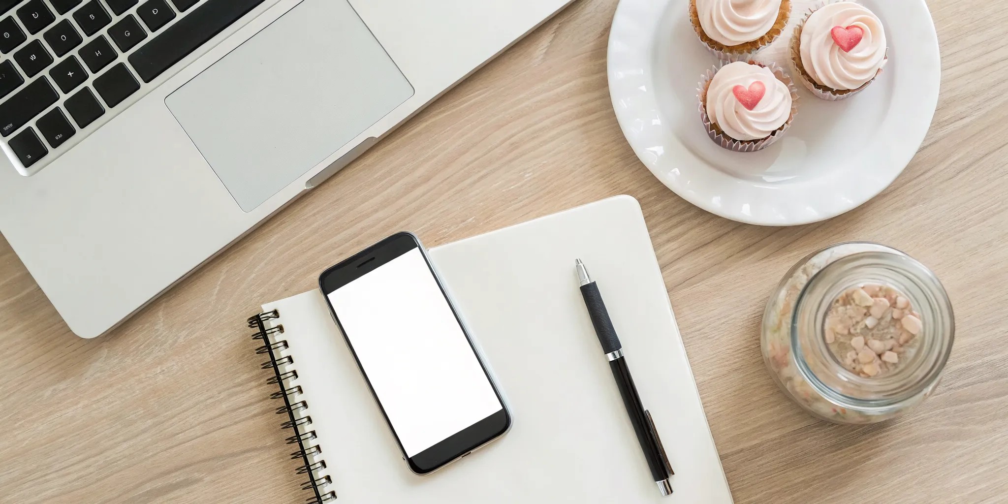 Planning creative fundraising ideas for individuals with a laptop, notebook, and cupcakes on a desk.